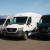 Three cargo vans including a silver RAM ProMaster, white Mercedes-Benz Sprinter, and black Ford Transit parked on a dealership lot under a clear sky